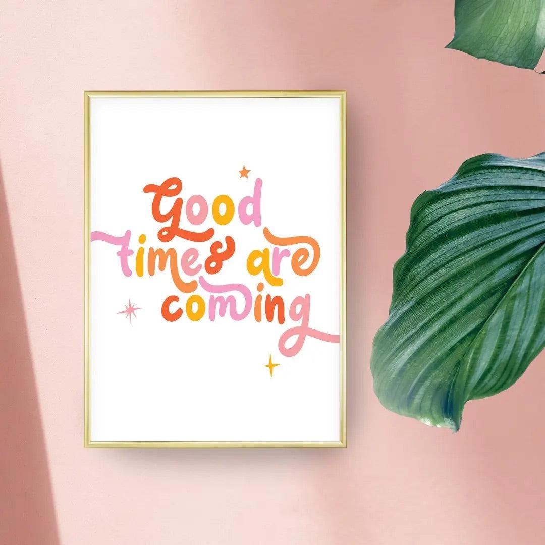 An A4 print with the words Good Times Are Coming in colourful lettering. the print is against a pink background with leaves peeking into the image.